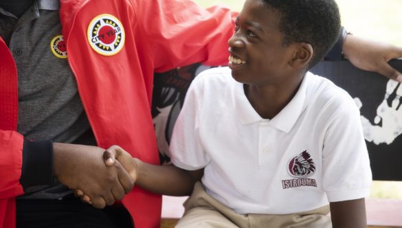 a young student smiles and looks up at an AmeriCorps member while shaking their hand