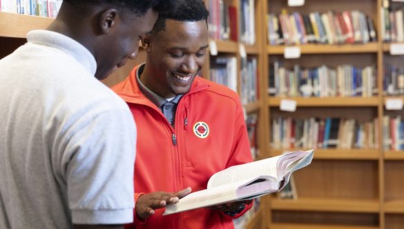 an AmeriCorps member is holding a book and reading with a student in the library