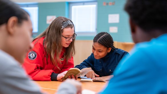 AmeriCorps member and students are reading a novel together at a table