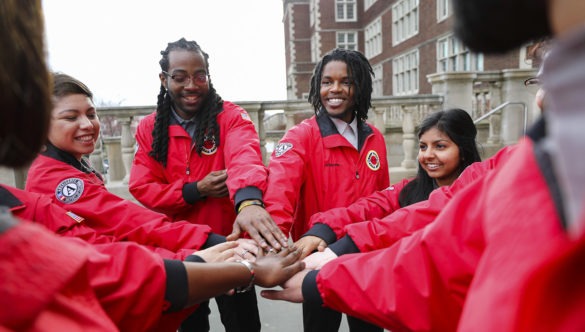 A team of City Year AmeriCorps members stand with their hands in the center of a circle, ready to do a spirit break