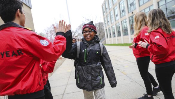 An elementary school student wearing glasses high fives a City Year AmeriCorps member outside their school