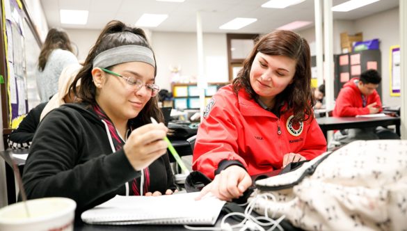 AmeriCorps member is pointing out something on high school student's page as they do work in the classroom