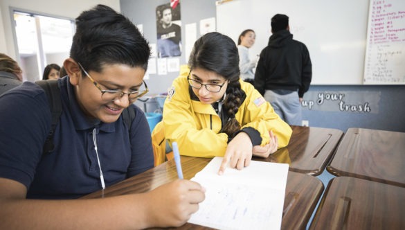 An AmeriCorps members sits at a desk with a student, pointing at his worksheet