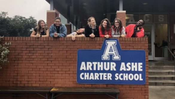 A team of seven AmeriCorps members lean over a brick wall smiling at the Arthur Ashe Charter school