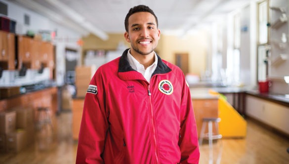 AmeriCorps member stands and smiles in the front of a school science lab.