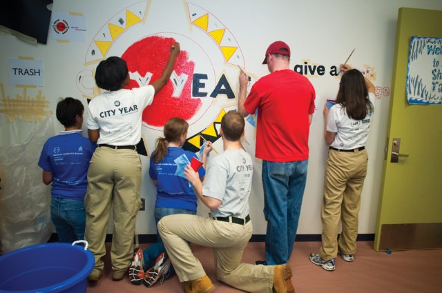 A group of AmeriCorps members and volunteers work on painting a school mural.