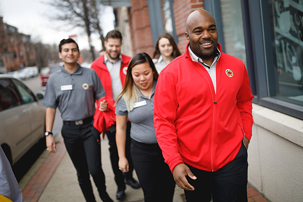 A group of AmeriCorps members and staff walk in a group on the side walk and share a laugh.