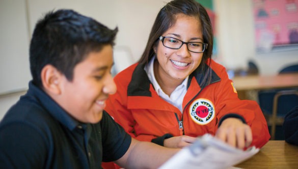 city year americorps member with a student sitting at a desk as they read together from the same paper