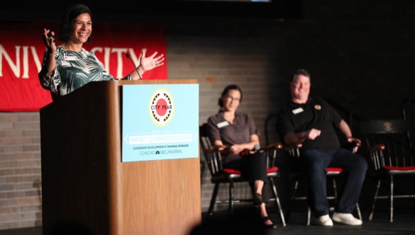 Mithra stands at a podium, speaking to a crowd of City Year's senior leaders